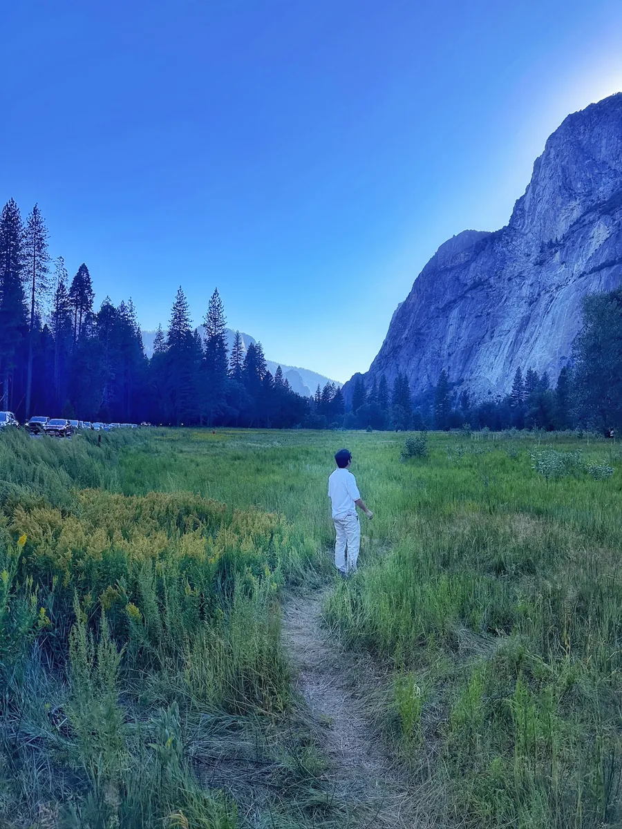 Akshay walking a footpath through a Yosemite meadow toward granite cliffs