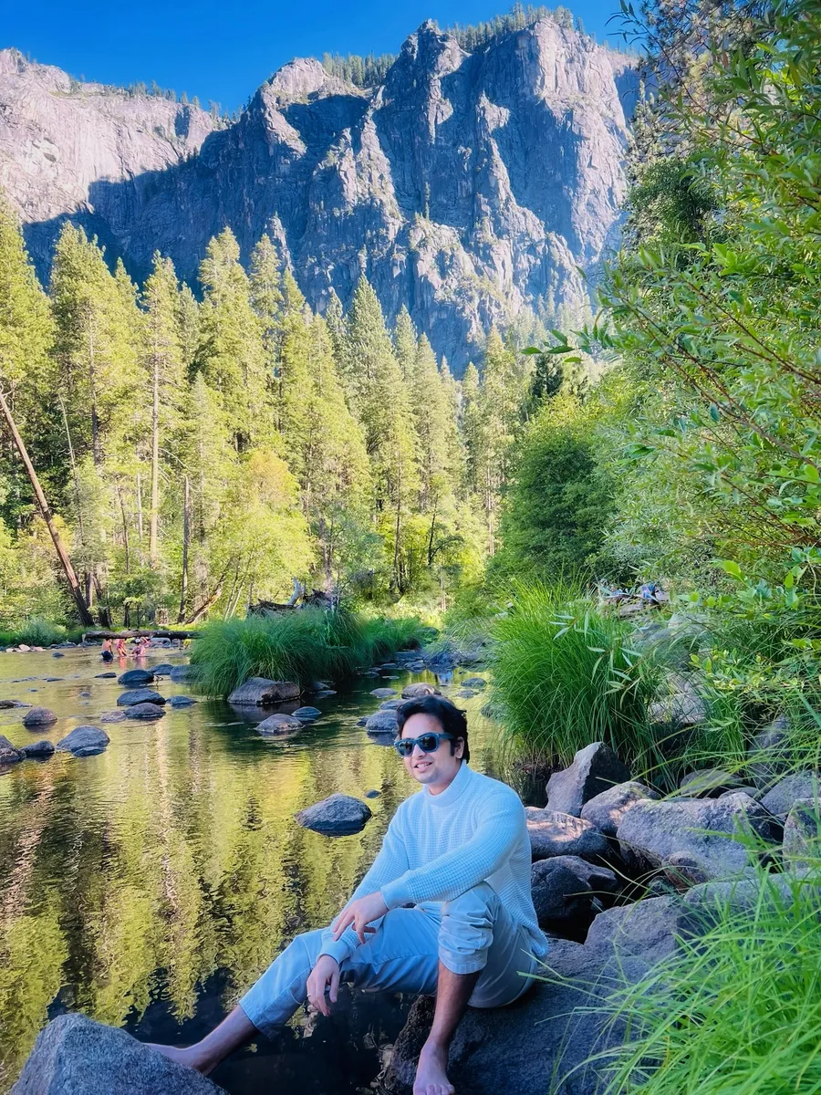 Akshay sitting on rocks by a river beneath Yosemite’s granite peaks